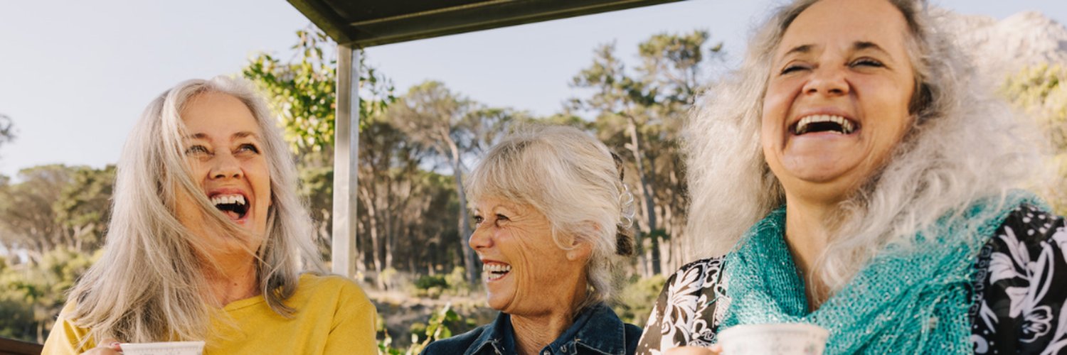 Three women laughing together over a cup of tea